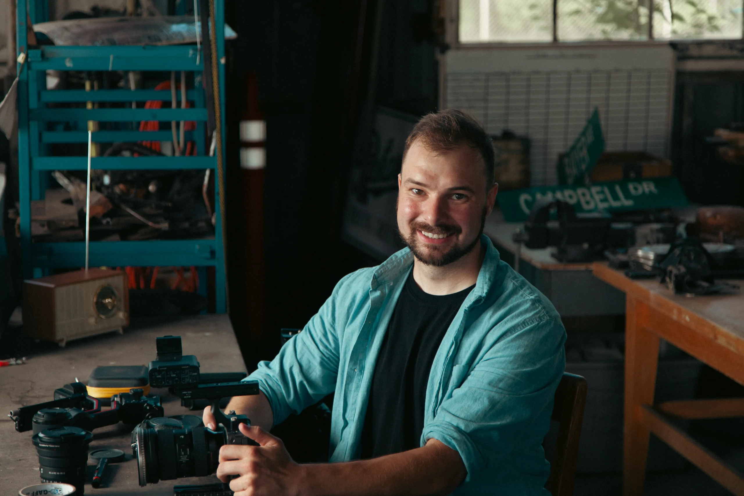 Ethan seated at a workbench with camera bodies and lenses laid out in front of him
